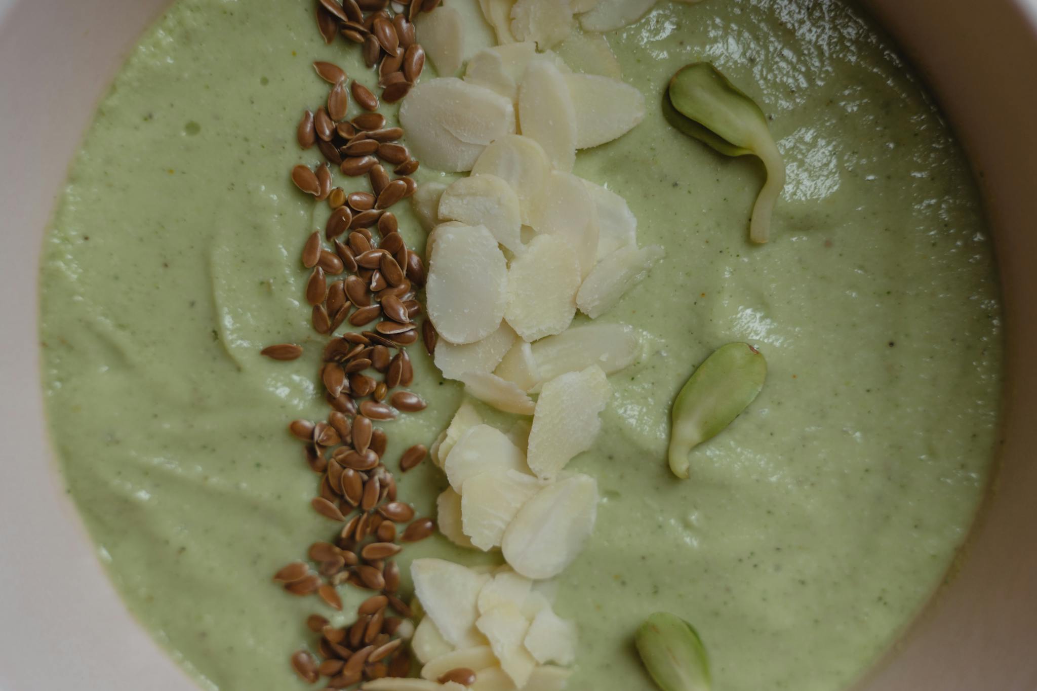 A vibrant green smoothie bowl garnished with flax seeds, almonds, and pumpkin seeds.