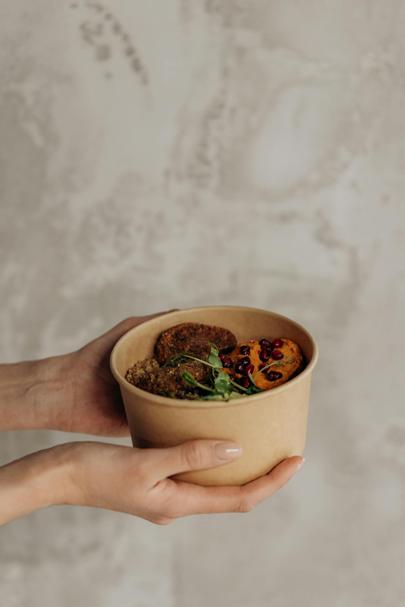 Close-up of hands holding a vegan bowl with quinoa, greens, and pomegranate.