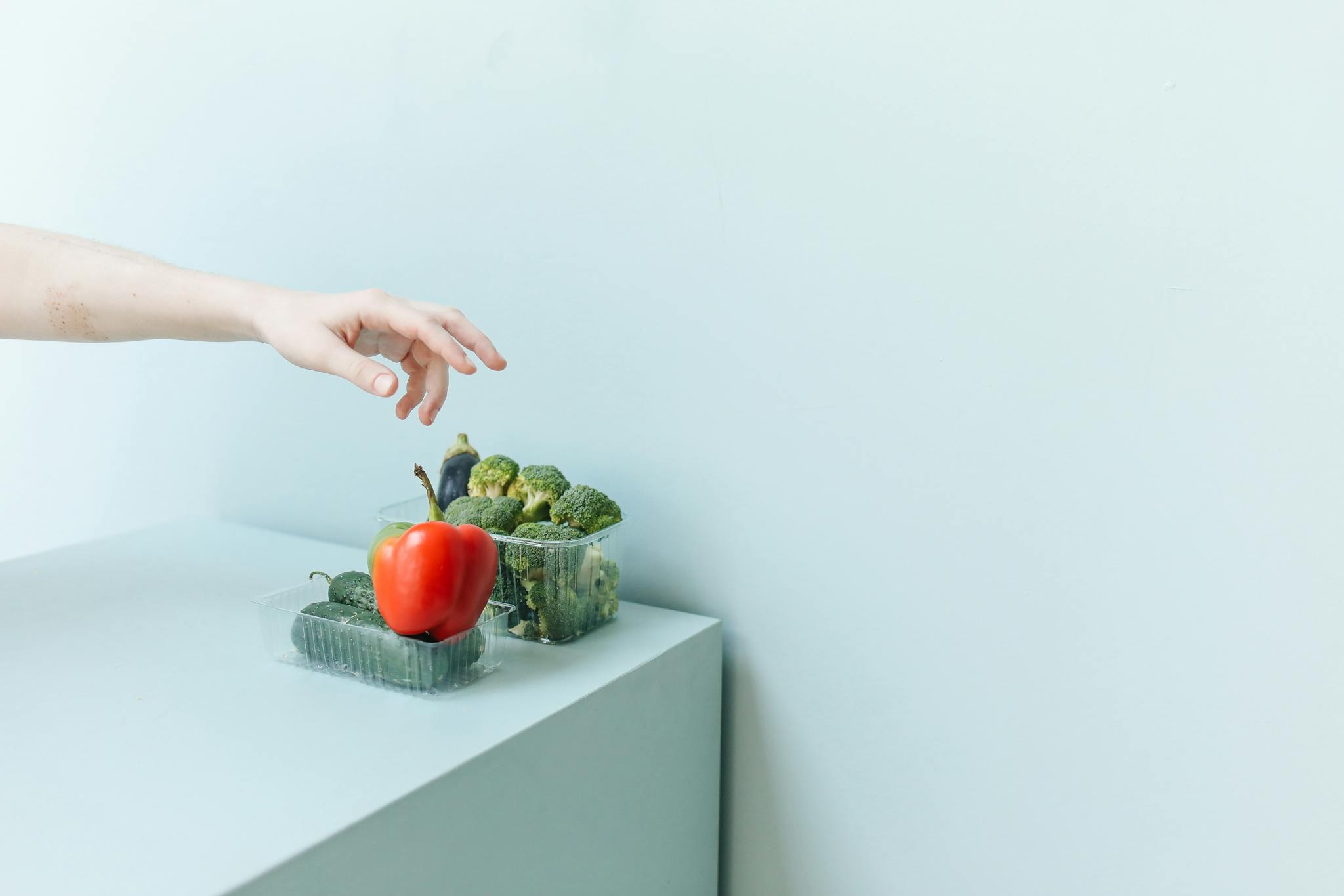 Hand reaching for fresh vegetables on a minimalist white surface.