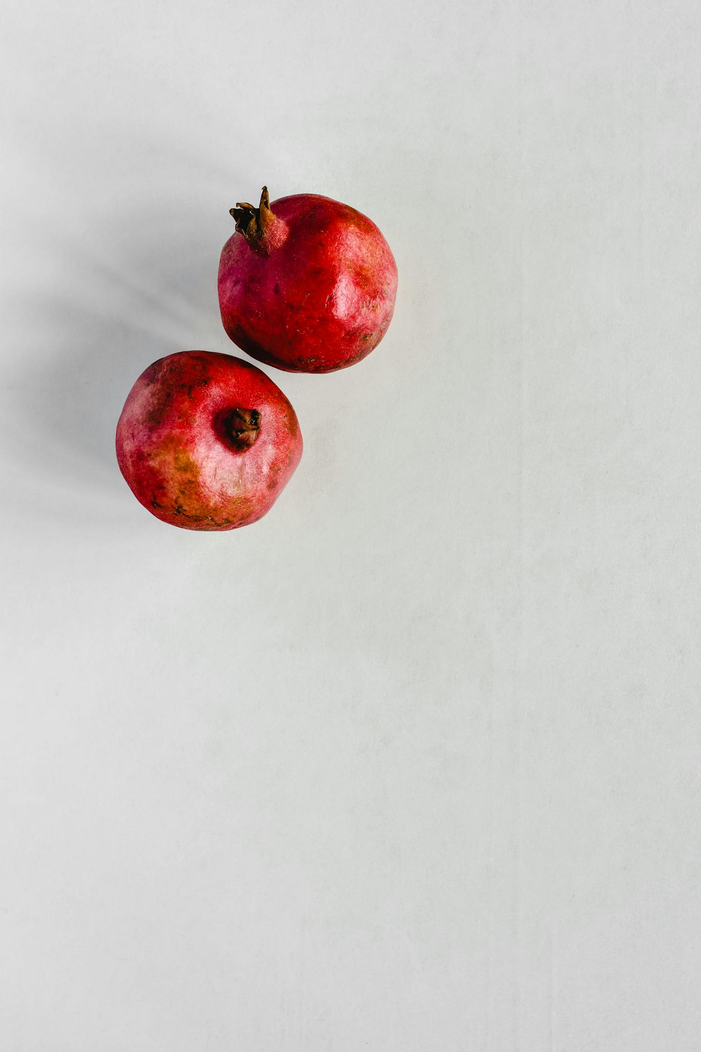 Two ripe pomegranates on a clean white surface, offering a minimalist look.